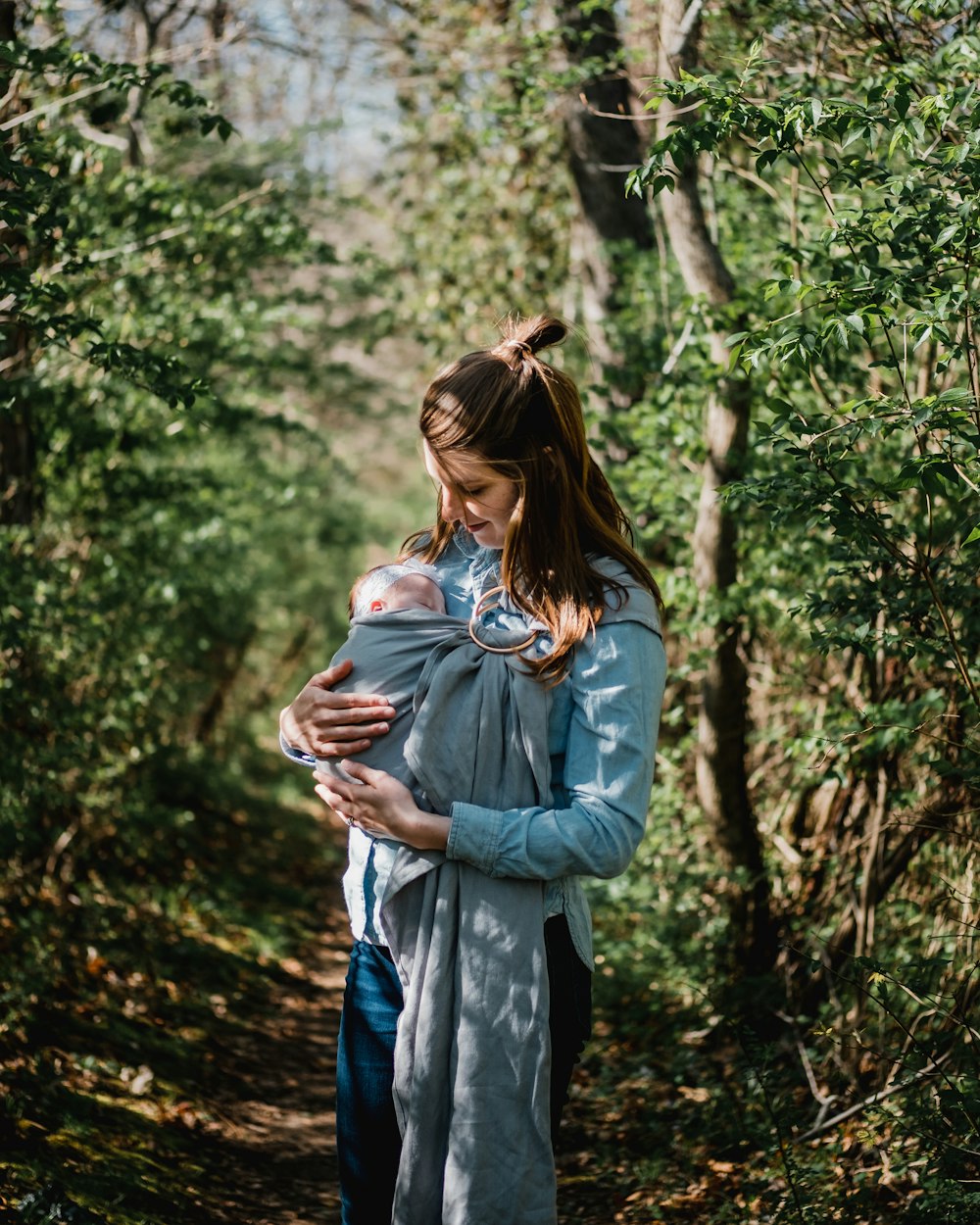 woman carrying child while standing near trees at daytime