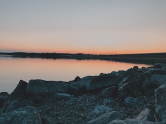 A sunset view over a serene lake with a silhouette of a frog-shaped rock in the foreground.