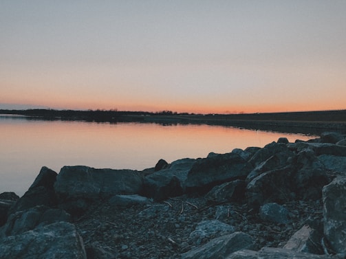 A sunset view over a serene lake with a silhouette of a frog-shaped rock in the foreground.