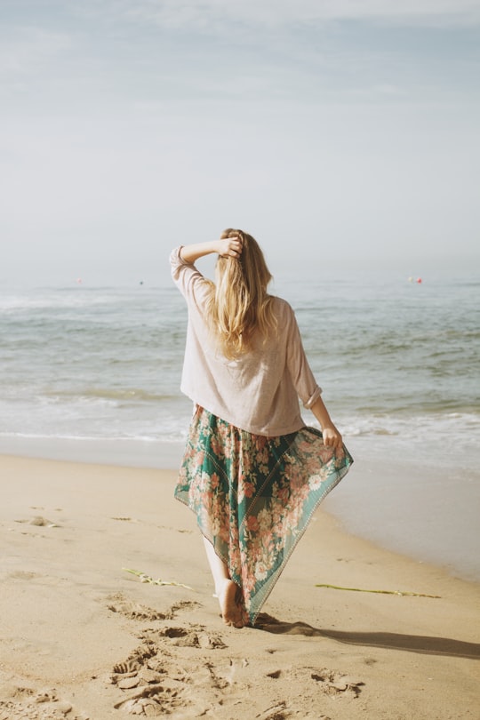 woman holding her skirt with her right arm and hair with left while standing on seashore in Huntington Beach United States