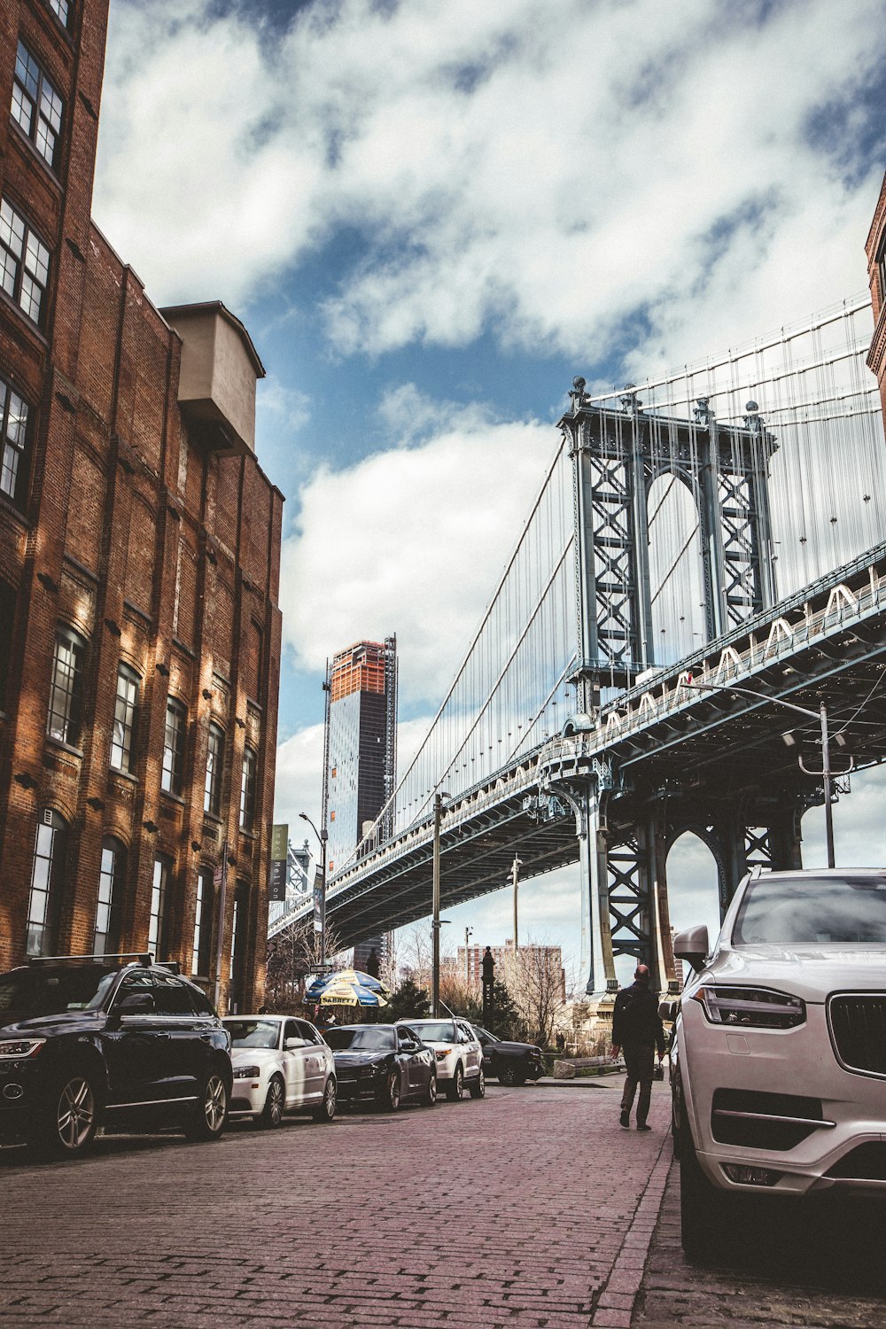 vehicles park on roadway near gray Manhattan bridge under white clouds during daytime