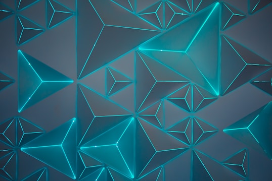 An array of three-dimensional geometric shapes featuring triangular pyramids arranged in a symmetrical pattern. The shapes have a glowing cyan outline, creating a futuristic and dynamic visual effect against a dark background.