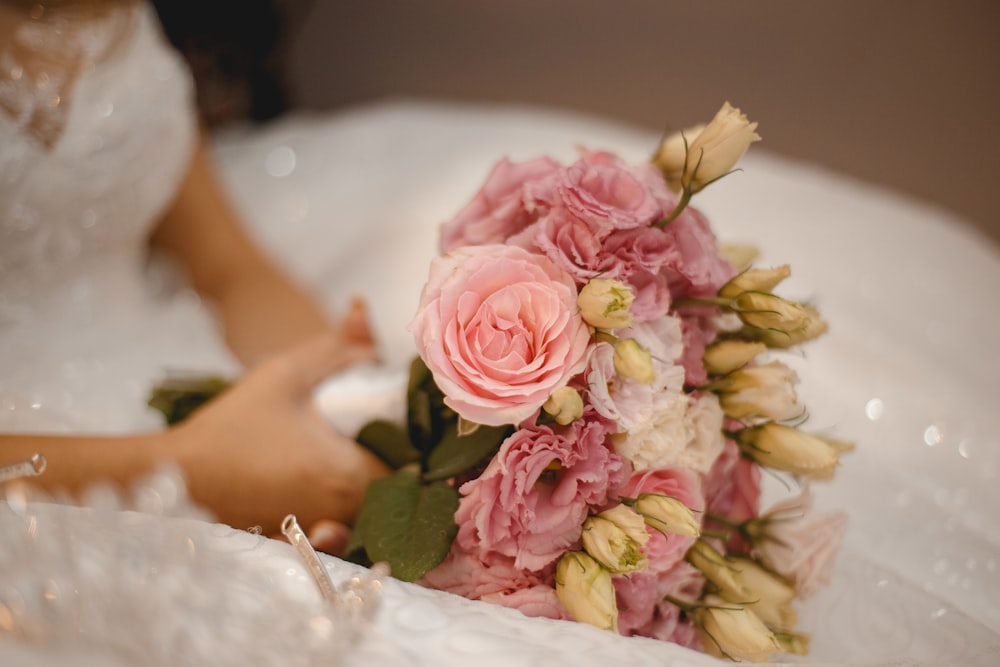 mujer en vestido de novia blanco sosteniendo ramo de flores rosas y blancas