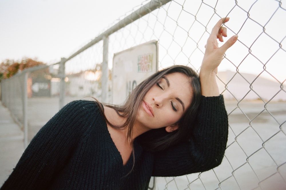 woman in black long-sleeved top holding on cyclone fence