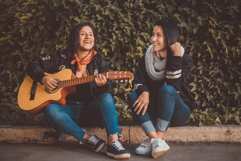 woman playing guitar sitting beside with woman wearing scarf