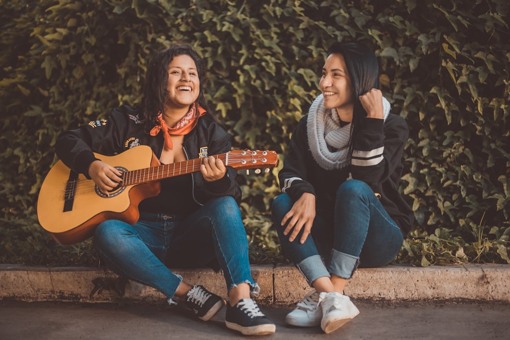 Mujer tocando la guitarra sentada al lado con la mujer que lleva bufanda