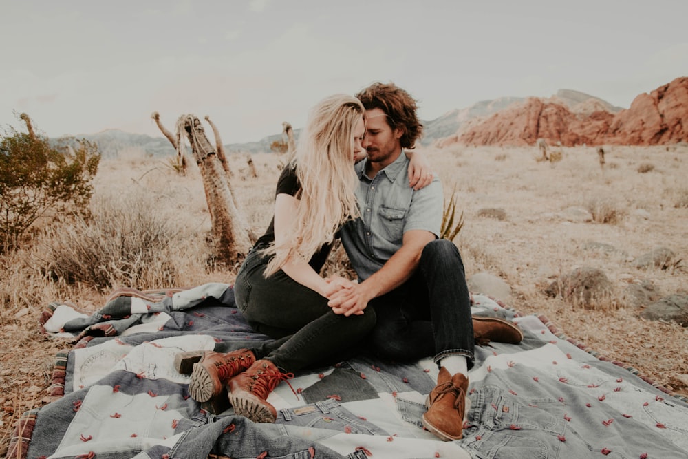 man and woman sitting on blanket while holding each other hands