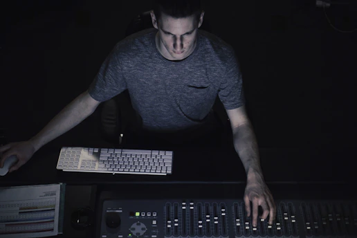 A music producer working intently at a mixing console surrounded by studio equipment.