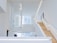 An interior space with a modern, minimalist design characterized by clean lines and open areas. A prominent wooden staircase with built-in lighting leads to the upper floors, surrounded by white walls and large windows that allow natural light to flood the space.