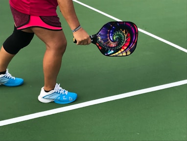 person showing pair of blue-and-white shoes with a pickleball paddle