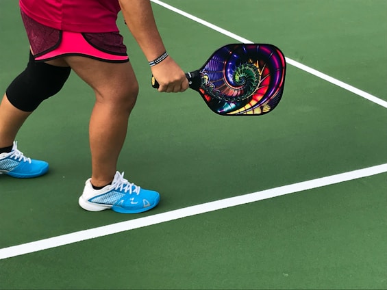 person showing pair of blue-and-white shoes with a pickleball paddle