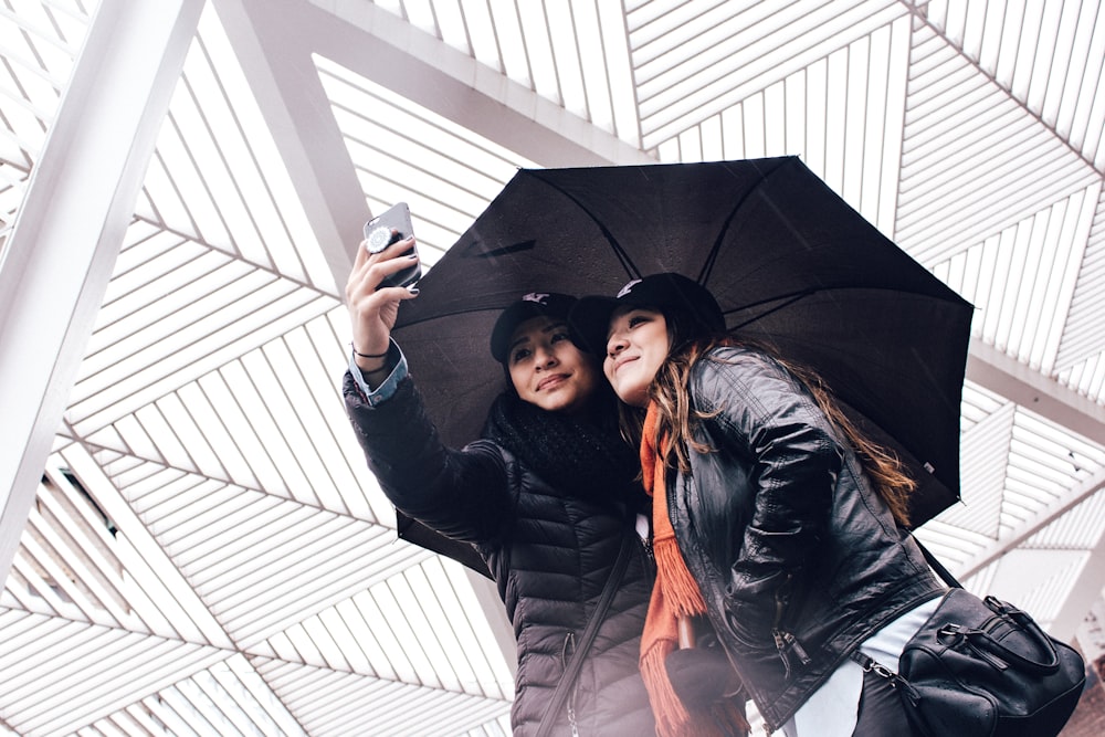 Zwei Frauen benutzen Regenschirm, während sie Selfie machen