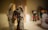 A detailed figurine of a powerful, muscular character with large, intricate wings, wearing dark armor with metallic accents, stands prominently in the foreground. The background is softly blurred, featuring dimly visible objects including another figurine and a plush toy.
