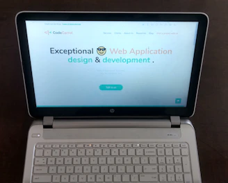 A laptop computer with a website displayed on the screen featuring the text 'Exceptional Web Application design & development'. The laptop is on a dark surface, and the website has a clean and modern design with a light background and colorful text elements.