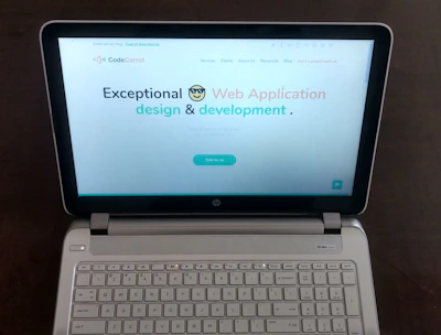 A laptop computer with a website displayed on the screen featuring the text 'Exceptional Web Application design & development'. The laptop is on a dark surface, and the website has a clean and modern design with a light background and colorful text elements.