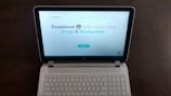 A laptop computer with a website displayed on the screen featuring the text 'Exceptional Web Application design & development'. The laptop is on a dark surface, and the website has a clean and modern design with a light background and colorful text elements.