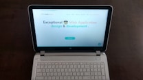 A laptop computer with a website displayed on the screen featuring the text 'Exceptional Web Application design & development'. The laptop is on a dark surface, and the website has a clean and modern design with a light background and colorful text elements.
