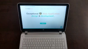A laptop computer with a website displayed on the screen featuring the text 'Exceptional Web Application design & development'. The laptop is on a dark surface, and the website has a clean and modern design with a light background and colorful text elements.