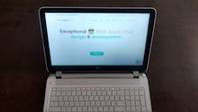 A laptop computer with a website displayed on the screen featuring the text 'Exceptional Web Application design & development'. The laptop is on a dark surface, and the website has a clean and modern design with a light background and colorful text elements.