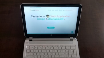 A laptop computer with a website displayed on the screen featuring the text 'Exceptional Web Application design & development'. The laptop is on a dark surface, and the website has a clean and modern design with a light background and colorful text elements.