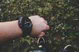 A wrist wearing a bold, square-faced watch paired with a casual outfit outdoors.