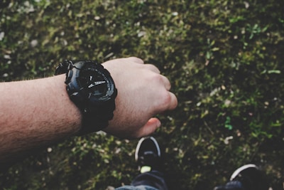 A wrist wearing a bold, square-faced watch paired with a casual outfit outdoors.