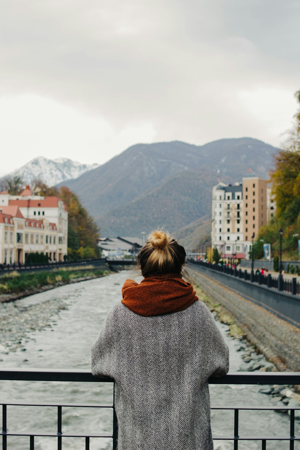 woman in gray coat leaning on metal bridge rail