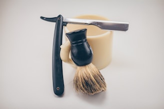 Vintage straight razor and shaving brush resting on a black marble countertop with golden accents.