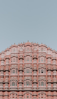 An intricate pink sandstone building featuring numerous ornate windows and arched designs. The architecture is symmetrical, showcasing detailed carvings and a historic style against a clear blue sky.