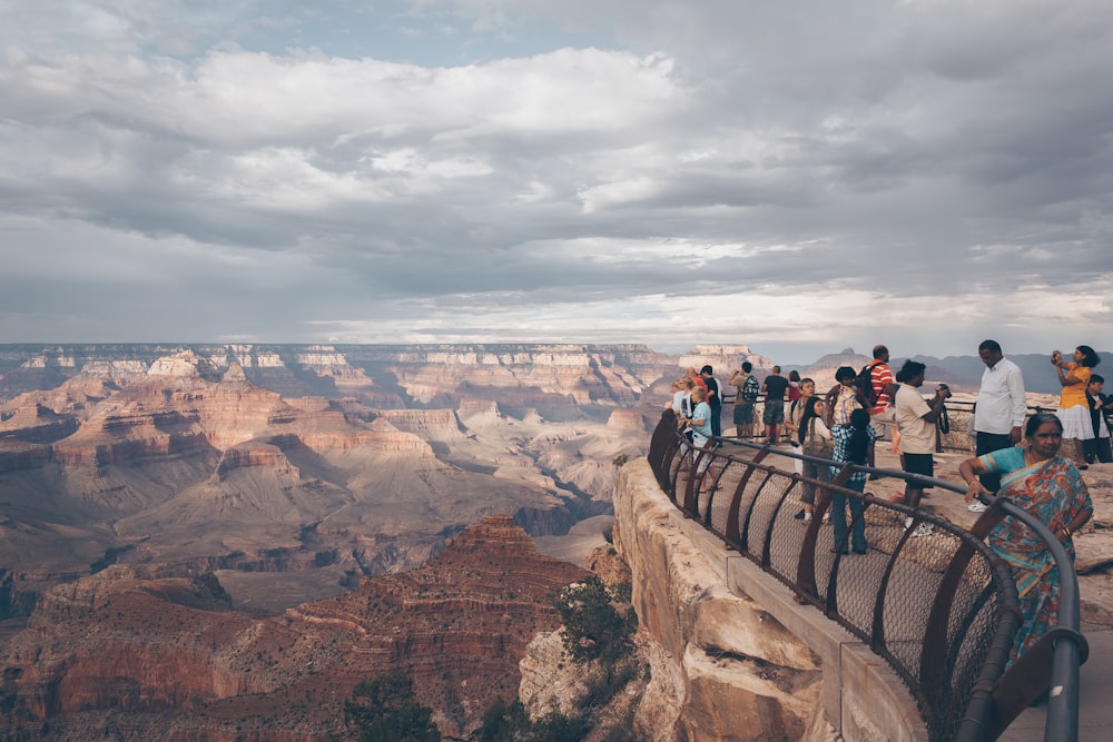 group of people standing at the top of cliff with railing