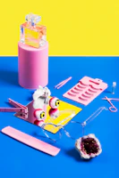 A cheerful flat lay of sunglasses, watches, and perfumes with splashes of bright colors around them.