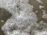 Foamy white bubbles spread unevenly across a wet sandy surface.