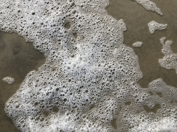 Foamy white bubbles spread unevenly across a wet sandy surface.