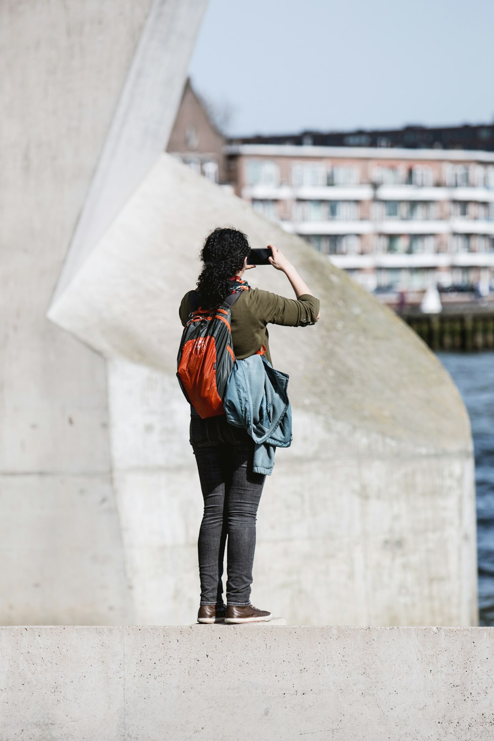 person standing on concrete edge holding up smartphone taking photo