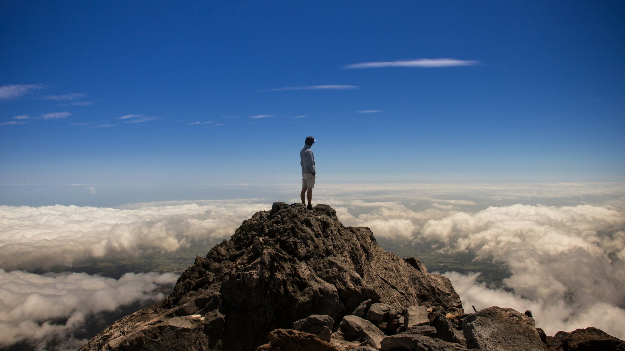 a solitary figure standing on a peak and looking over a layer of clouds