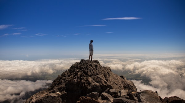 a solitary figure standing on a peak and looking over a layer of clouds