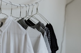 Several clothes are hanging on wire hangers, including a white button-up shirt and a variety of gray and black t-shirts. The setting appears minimalistic with a muted color scheme.