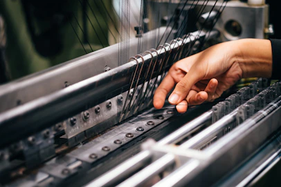 Close-up of hands working on textile machinery with colorful threads.