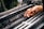 A hand is carefully operating a complex piece of machinery, involving several metal rods and strings, likely part of a textile manufacturing process.