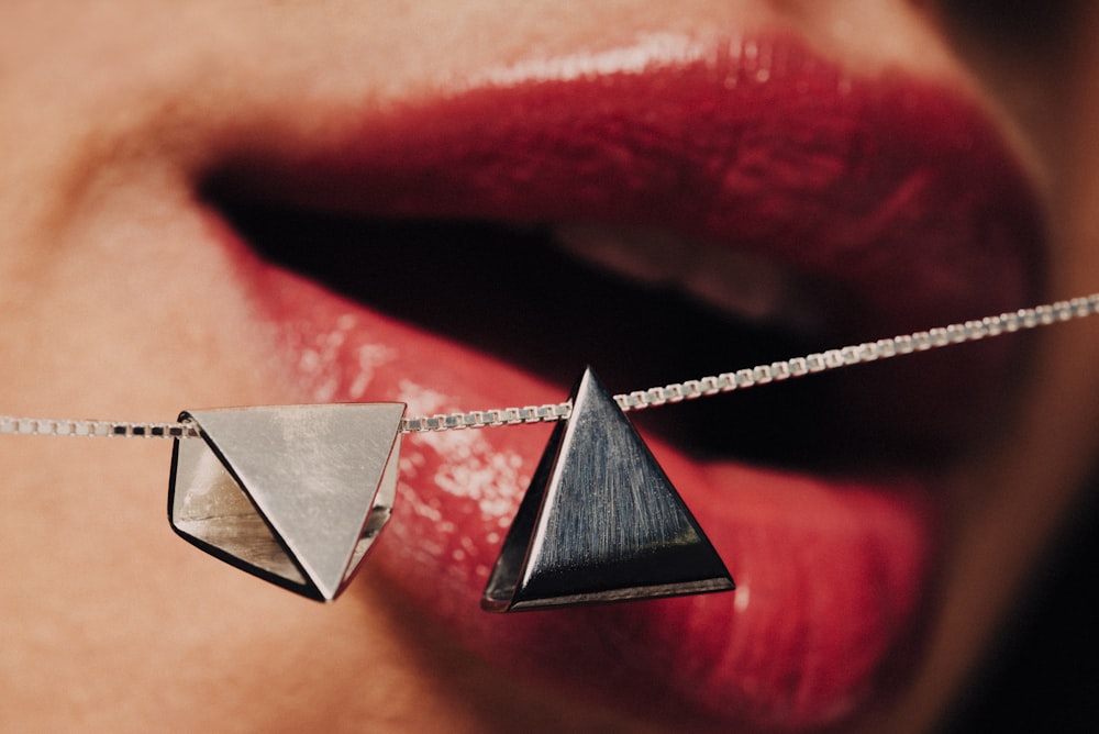 silver-colored necklace with triangle pendant near woman's mouth