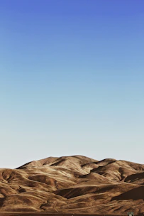Rolling rural land with open fields and distant tree lines under a blue sky.
