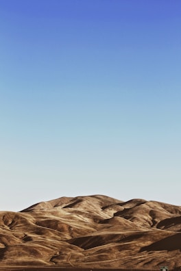 Rolling hills with a smooth, undulating terrain stretch across the landscape under a clear, blue sky.