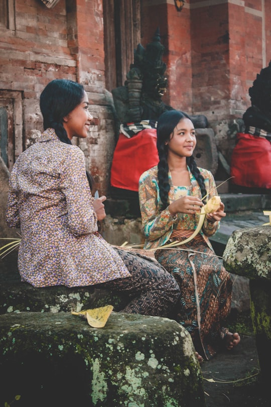 woman holding woven coconut leaf beside woman sitting while holding knife in Tenganan Indonesia