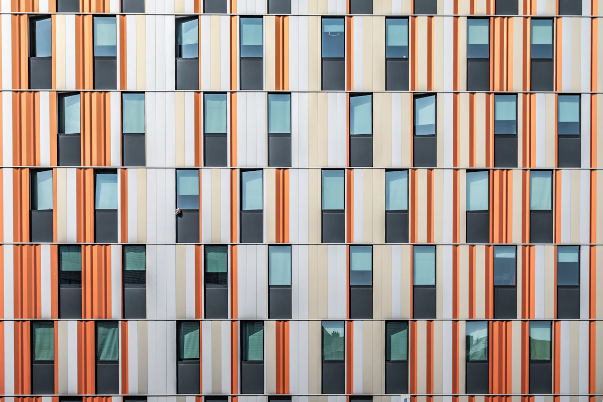 A modular building facade of repeating window bays in orange and cream, used as a campus signage grid reference
