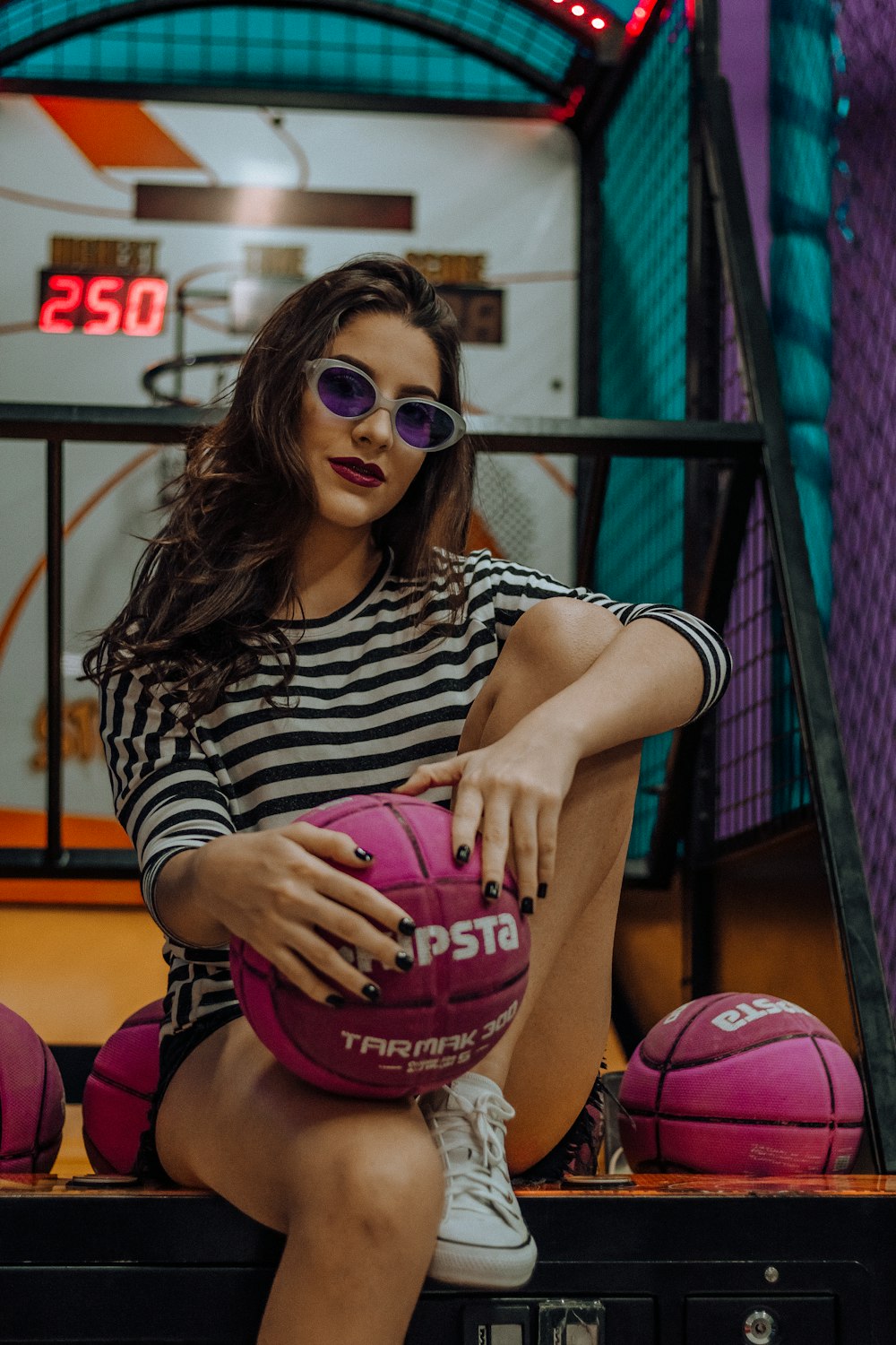 Frau im schwarz-weiß gestreiften Hemd sitzt auf Basketball-Arcade-Automat