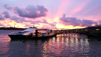 Sunset view of a luxury yacht docked at Cabo San Lucas marina with vibrant colors reflecting on the water.