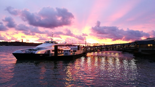 Sunset view of a luxury yacht docked at Cabo San Lucas marina with vibrant colors reflecting on the water.