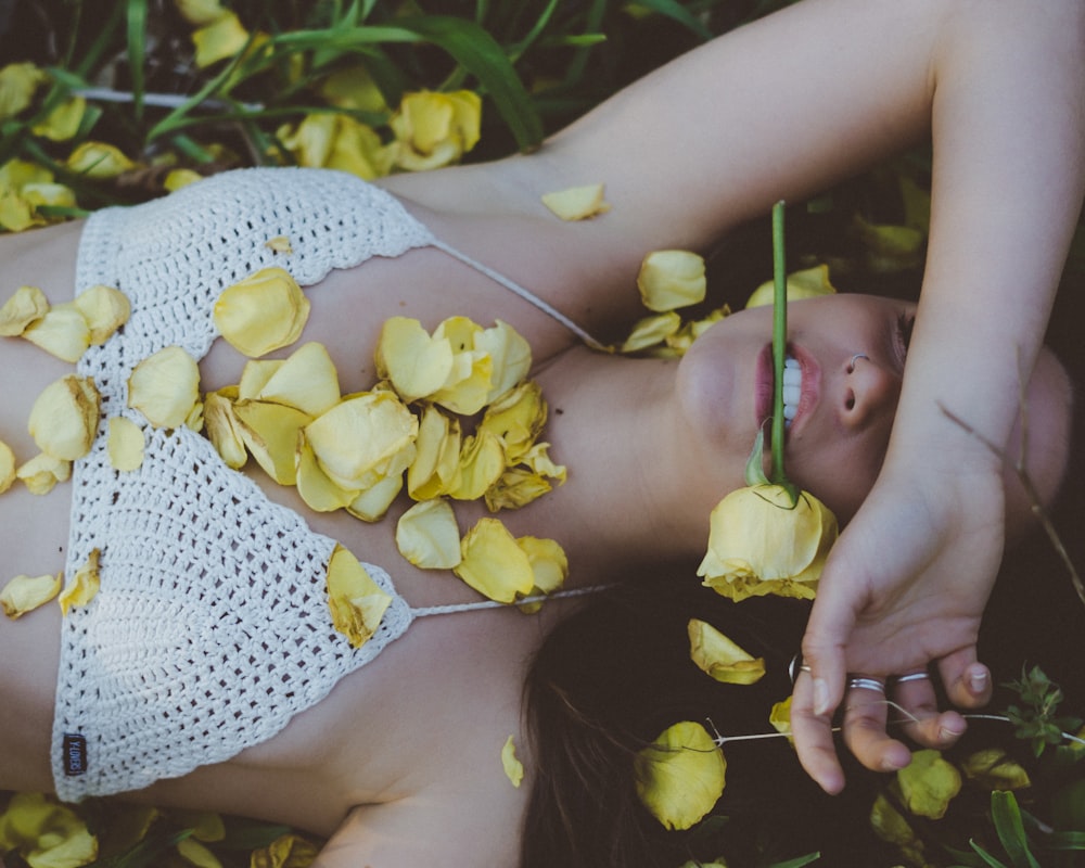 Frau liegt auf Pflanze mit gelber Blume im Mund