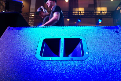A large professional speaker with multiple drivers, glowing softly in a dim event hall.