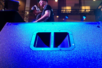 A large professional speaker with multiple drivers, glowing softly in a dim event hall.